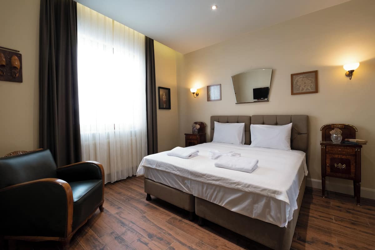 Ein Hotelzimmer mit einem großen Bett, einem Sessel, einem Nachttisch und einem Fenster mit Vorhängen.