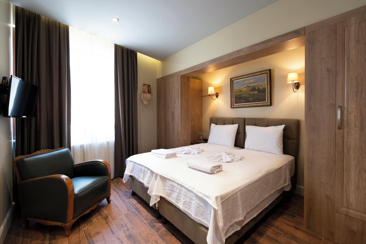 Ein Hotelzimmer mit einem großen Bett, einem Sessel, einem Fernseher und einem Bild an der Wand.