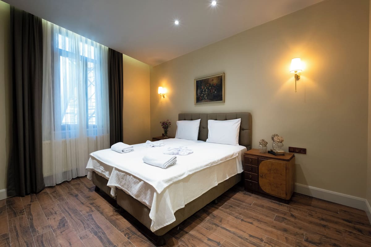 Ein ordentlich bezogenes Bett mit weißen Leinentüchern, ein Nachttisch aus Holz mit einer Lampe und ein Bild an der Wand.