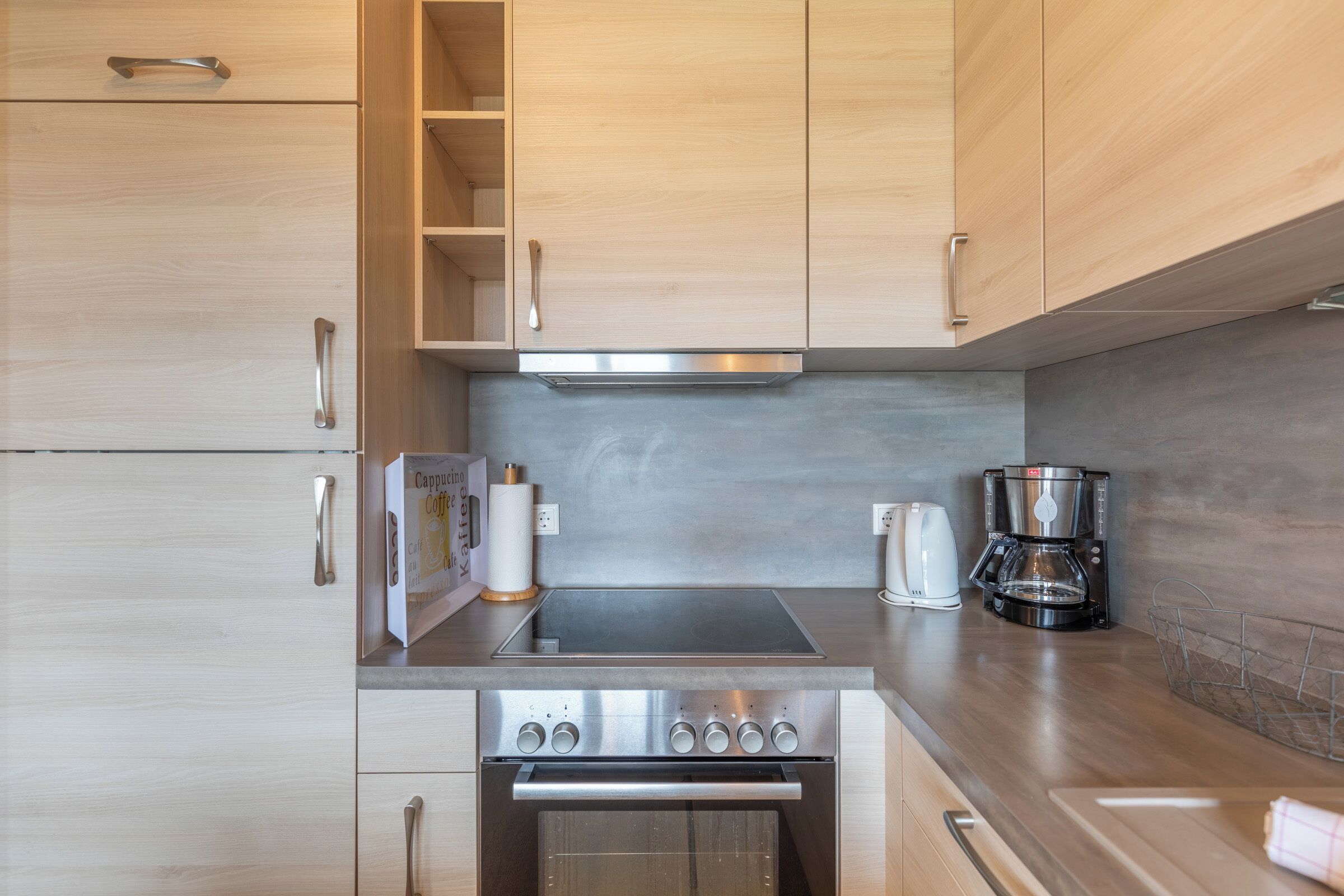 A modern kitchen with wooden cabinets, a stainless steel stove, and a coffee maker.