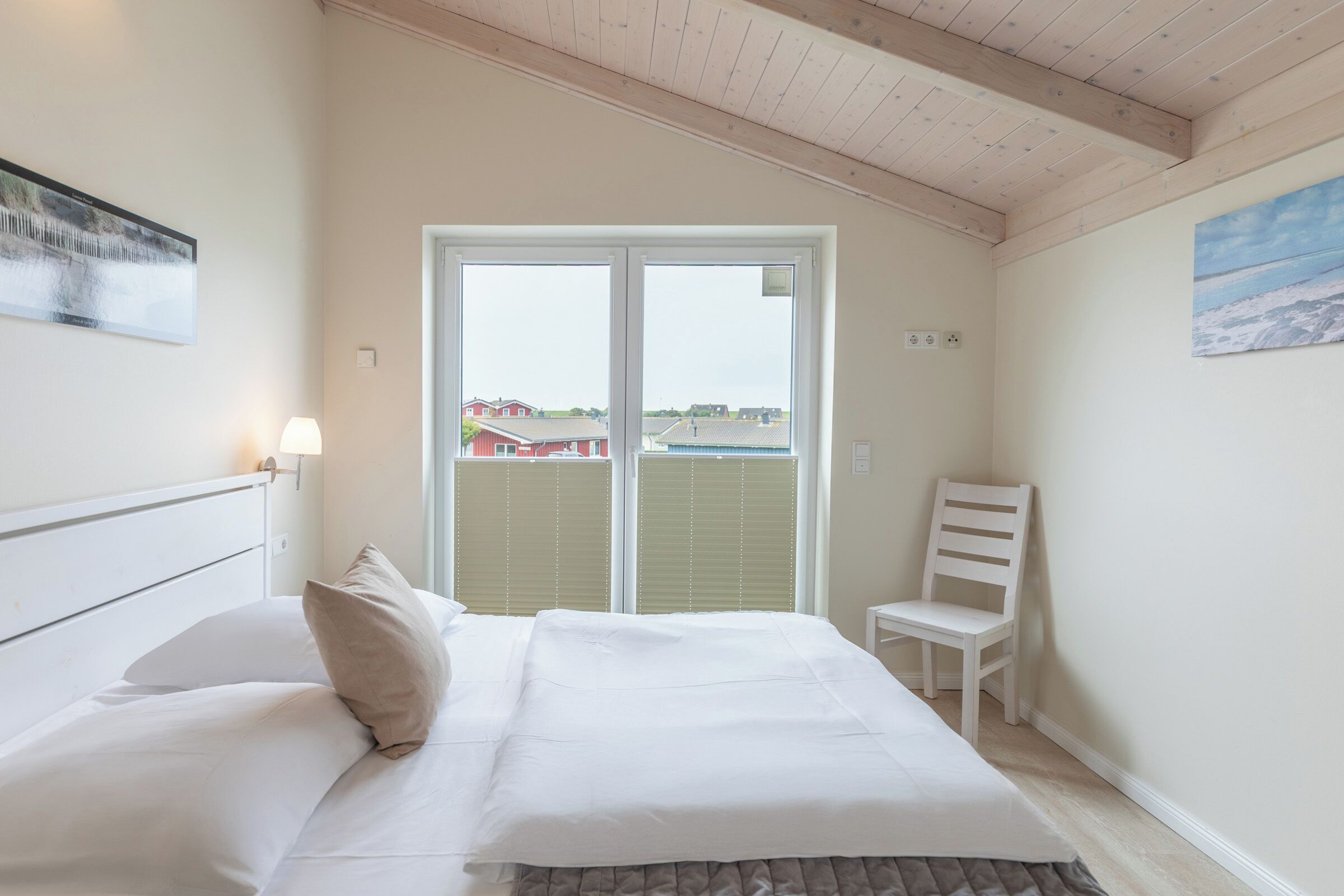 A bedroom with a bed, a chair, a window, and a painting on the wall.