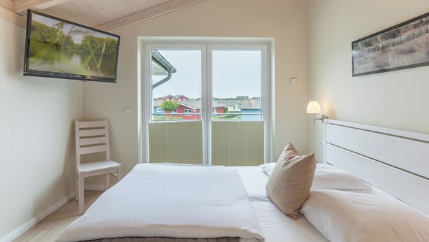 Een hotelkamer met een bed, een stoel, een aan de muur bevestigde televisie en een raam met uitzicht op huizen.