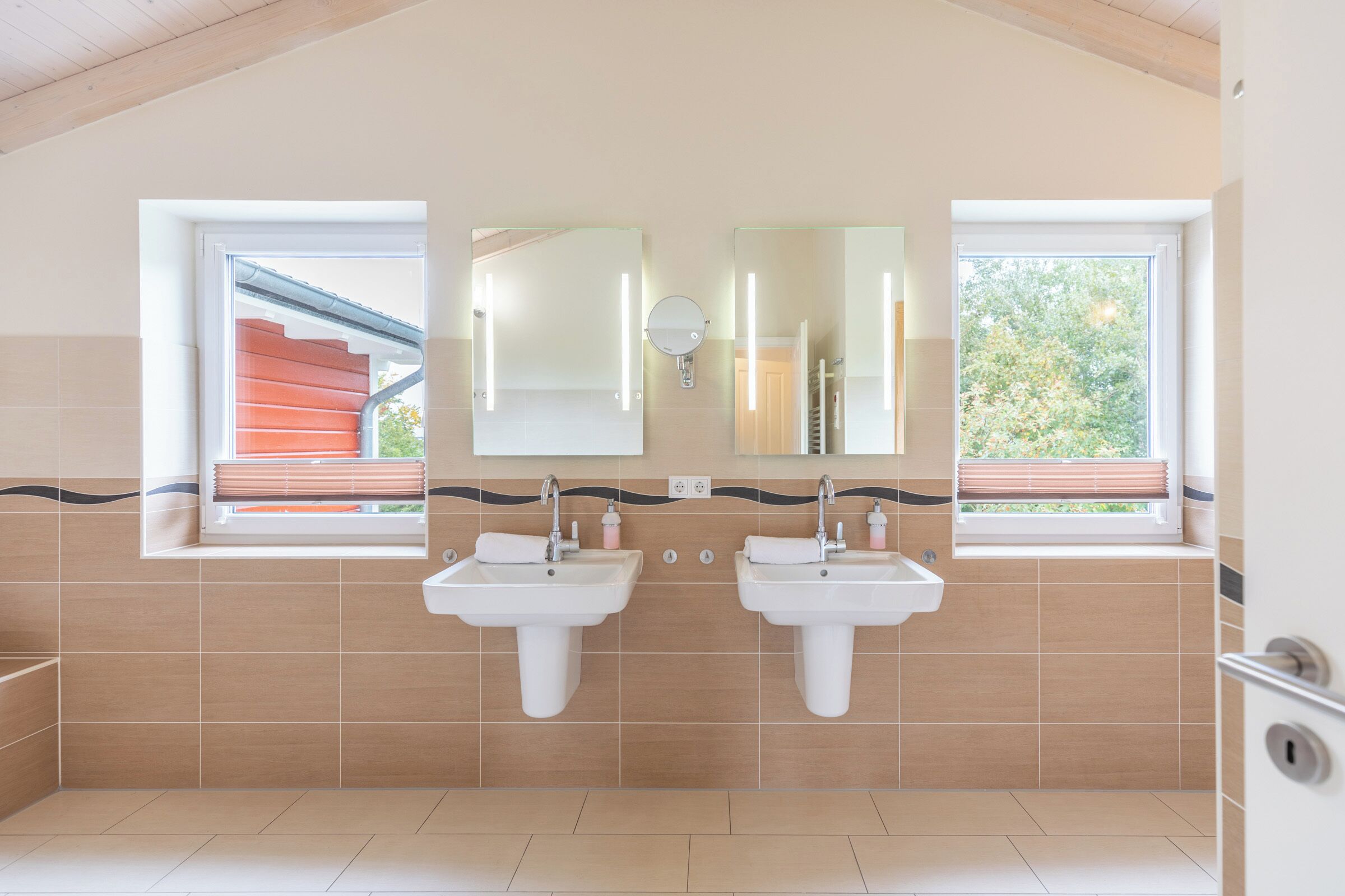 A bathroom with two sinks, a large mirror, and a window with a view of a red staircase and greenery outside.