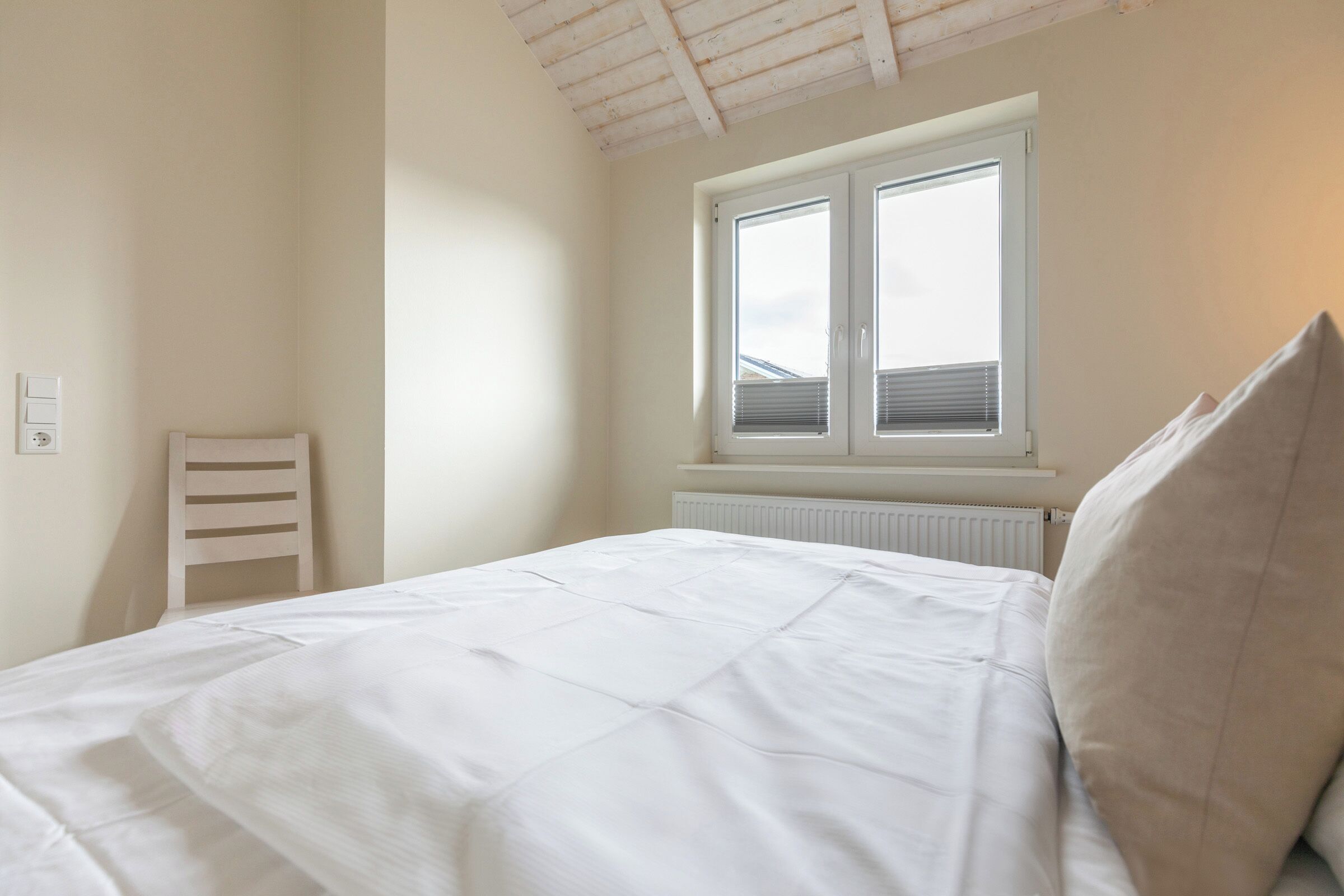 A bedroom with a bed, a window, a radiator, and a chair.