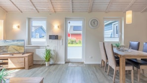 Tilava keittiö, jossa on puulattia, ruokailutila puupöydällä ja -tuoleilla, televisio ja ruukkukasvi.