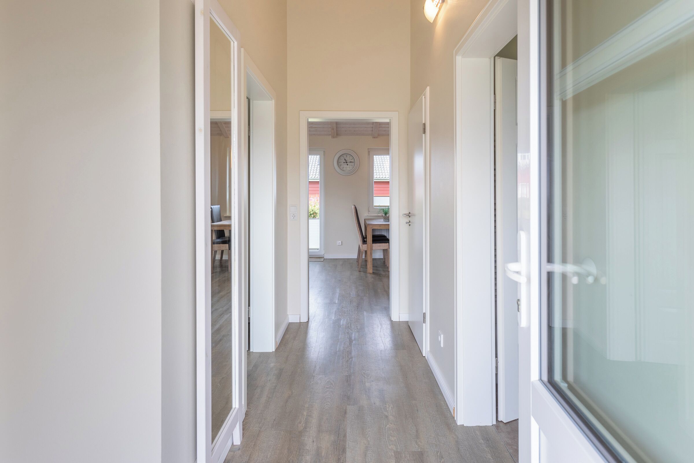 Ein Flur mit Holzboden, weißen Wänden und einer Tür zu einem Zimmer mit einem Fenster.