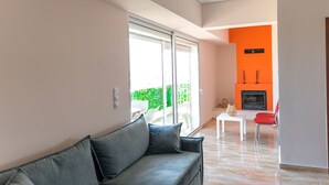 A modern living room with a grey sofa, a small white table, and a red chair. There is a glass door leading to a balcony with green plants. - Athens Acropolis View Penthouse-center of Athens (Athens)