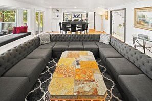 A modern living room with a sectional sofa, a coffee table with a mosaic top, and a dining area in the background. - Lakefront Splendor:Spectacular Lakefront Property w/Private Dock! Pool Table + Foosball Table! Spacious Outdoor Deck! Patio & Yard w/Firepit! (Big Bear Lake)