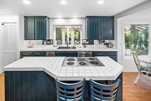 A modern kitchen with a central island, dark cabinetry, and a view of the outdoors. - Lakefront Splendor:Spectacular Lakefront Property w/Private Dock! Pool Table + Foosball Table! Spacious Outdoor Deck! Patio & Yard w/Firepit! (Big Bear Lake)