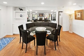 A modern dining area with a glass table surrounded by black chairs, a white floor rug, and a white wall with shelves. - Lakefront Splendor:Spectacular Lakefront Property w/Private Dock! Pool Table + Foosball Table! Spacious Outdoor Deck! Patio & Yard w/Firepit! (Big Bear Lake)