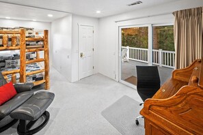 A room with a wooden bench, a black chair, a piano, and a door leading to a balcony. - Lakefront Splendor:Spectacular Lakefront Property w/Private Dock! Pool Table + Foosball Table! Spacious Outdoor Deck! Patio & Yard w/Firepit! (Big Bear Lake)