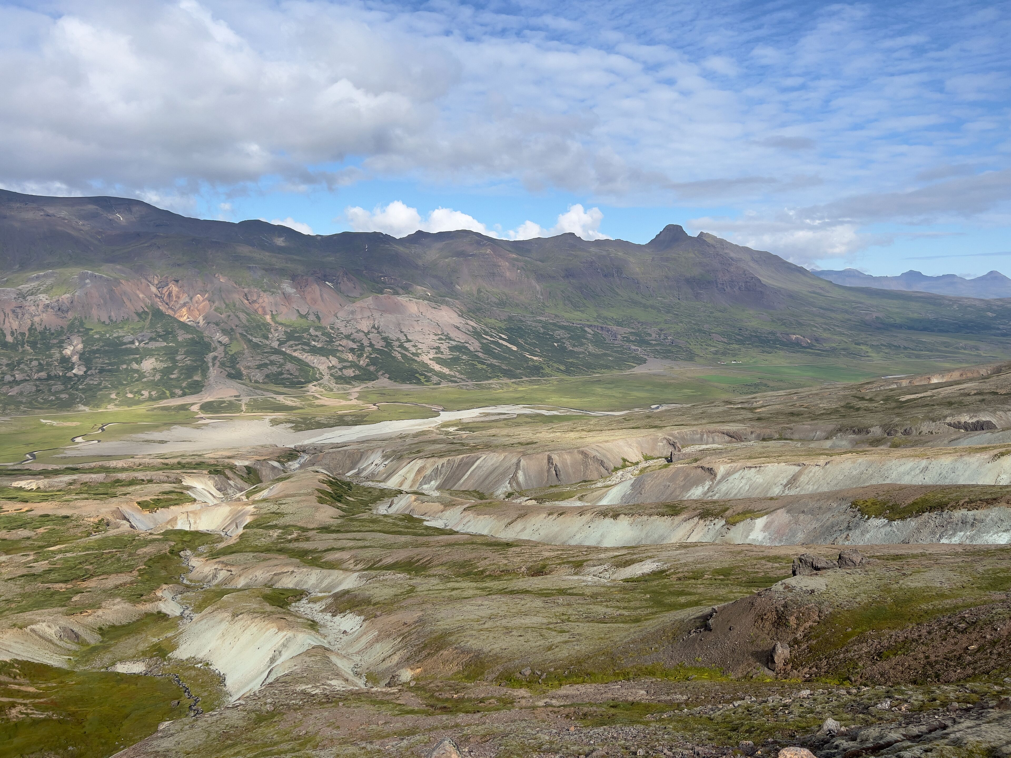 Un paisaje montañoso con un río, valles verdes y montañas a lo lejos.