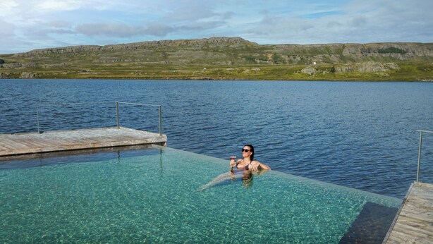 Una piscina limpida con un pontile in legno e una persona che si rilassa nell'acqua.