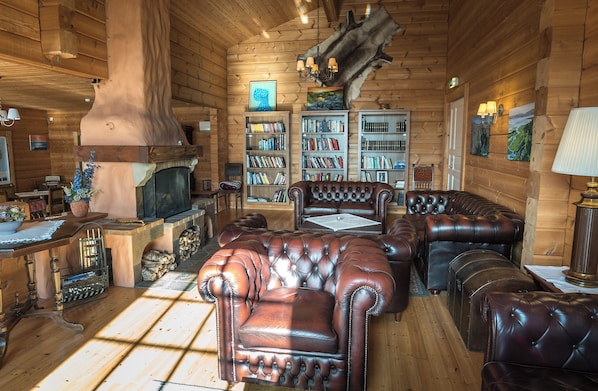 A log cabin interior with a fireplace, leather furniture, bookshelves, and a rustic decor. - Bjálki Cabin Lodge (Fjardabyggd)
