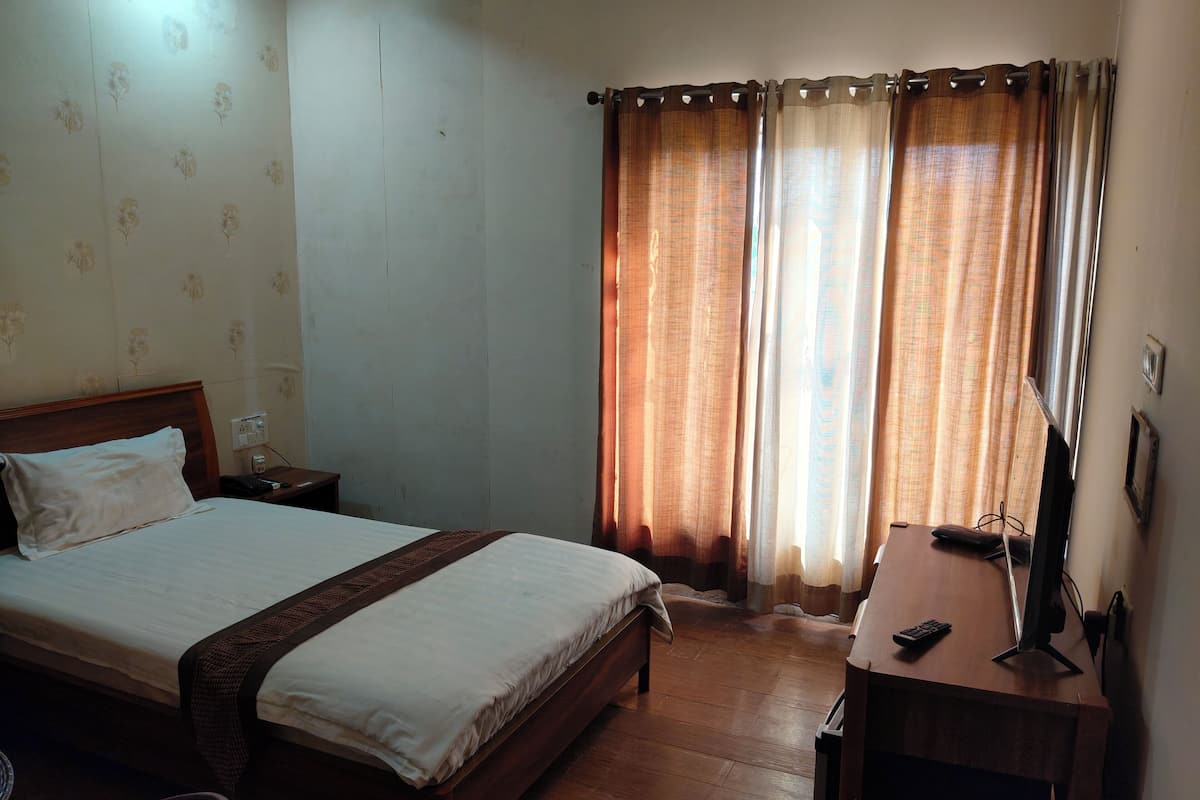 A hotel room with a bed, bedside table, lamp, and a desk with a computer.