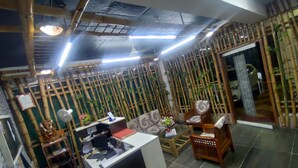 A room with a bamboo wall, a sofa, a wooden chair, a desk with a computer, and a fan. - Shavin Residency Wardha Maharashtra (Wardha)