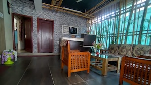 A spacious living room with a dark tiled floor, a wooden sofa set, a coffee table, and a TV on a wooden stand. There are two doors, one of which is open, revealing a hallway. - Shavin Residency Wardha Maharashtra (Wardha)