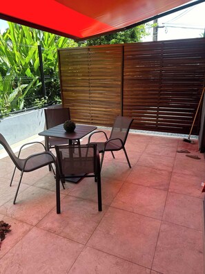 An outdoor patio with a table and chairs, a red canopy, and a wooden fence.