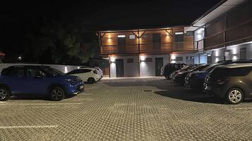 Ein Parkplatz mit mehreren Autos, ein Gebäude mit Holzfassade und mehreren Eingängen sowie befestigter Boden.