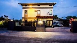 A two-story building with a gated entrance, a satellite dish, and a parking area with cars. - Value Inn Homestay by uBook (Butterworth)