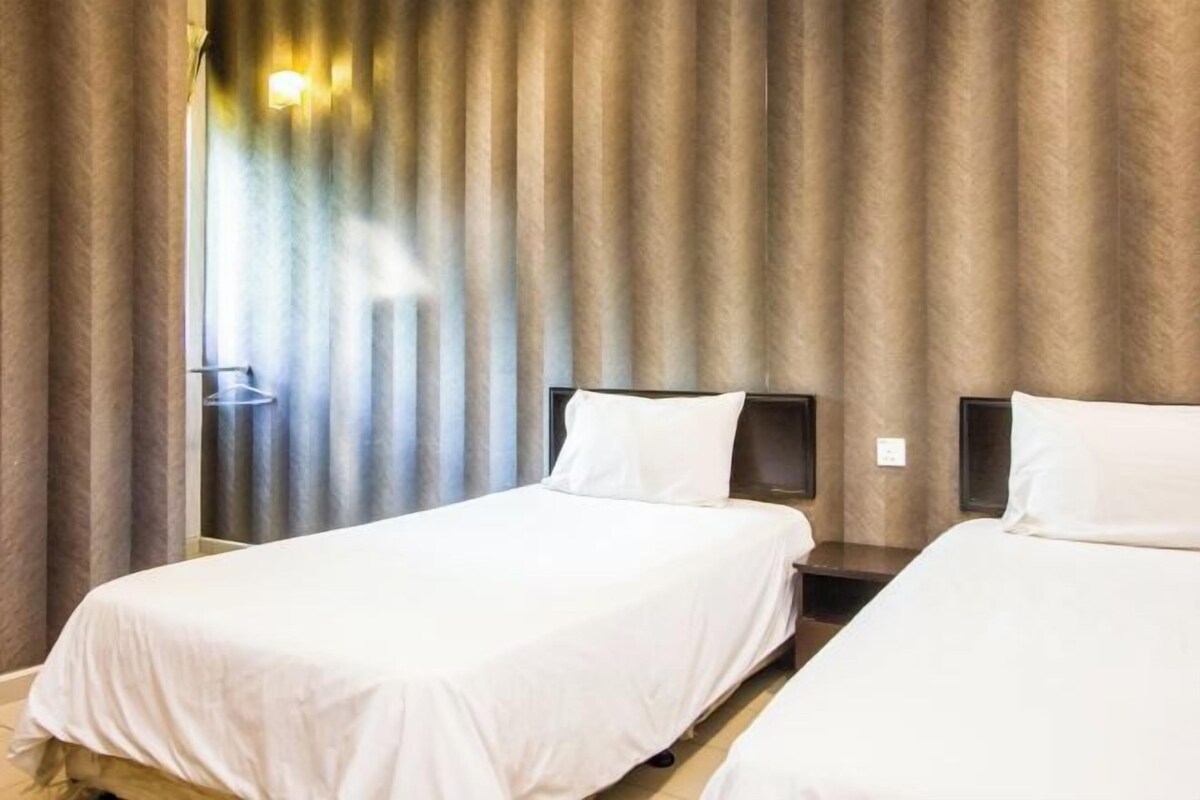 A hotel room with two beds, a nightstand, a lamp, and a window with curtains.