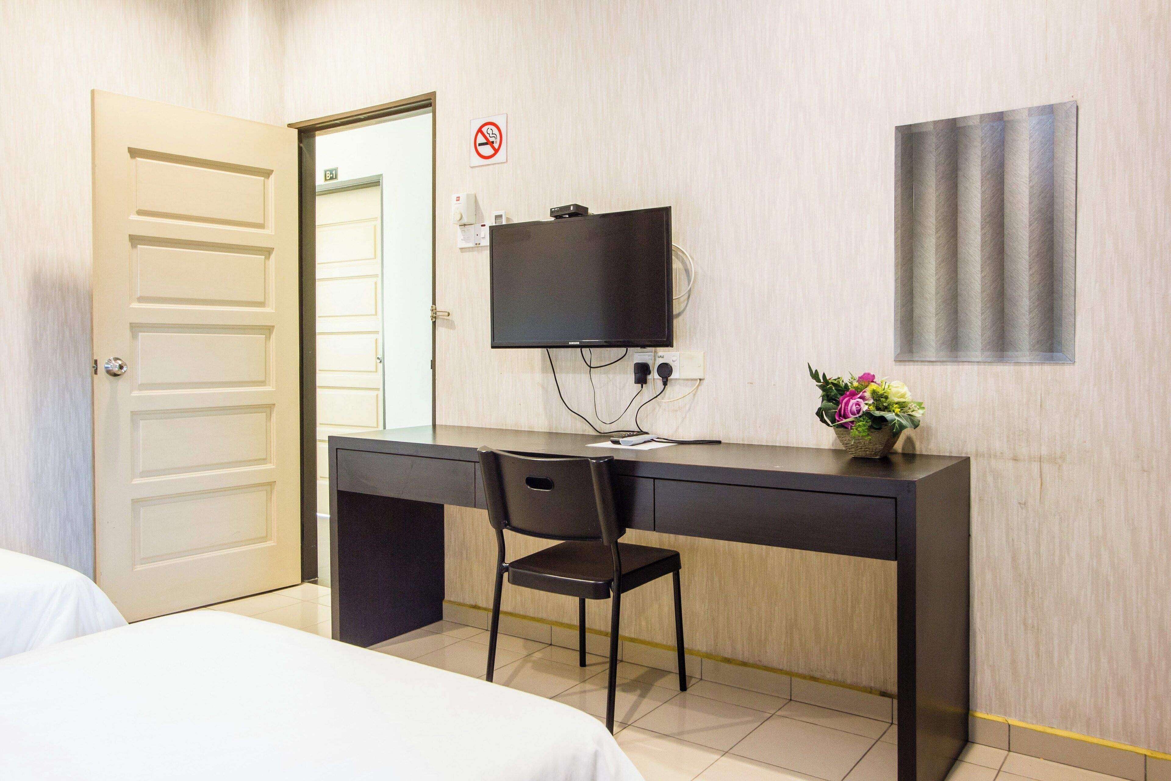 Una habitación de hotel con una cama, un escritorio con una silla, un televisor y un florero.