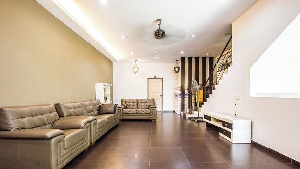 A spacious living area with a leather sofa, a smaller sofa, and a white console table. - Value Inn Homestay by uBook (Butterworth)