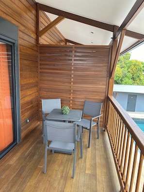 A wooden deck with a table and chairs, a view of a swimming pool, and a wooden railing. - Studio avec piscine (Cayenne)