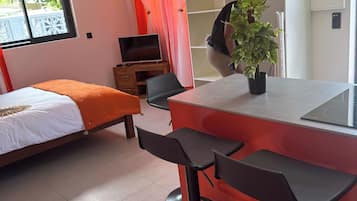 A modern room with a bed, a TV, a red and white color scheme, and a plant on the counter.