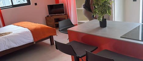 A modern room with a bed, a TV, a red and white color scheme, and a plant on the counter.