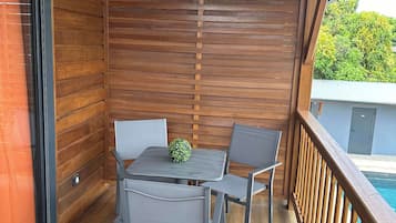 A wooden deck with a table and chairs, a view of a swimming pool, and a wooden railing.