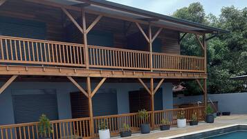 Un bâtiment en bois à deux étages, doté d’une piscine, d’une terrasse en bois et de plantes en pot.