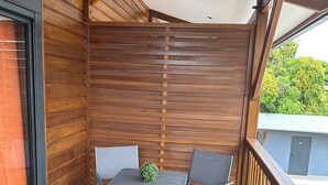 A wooden balcony with a table and chairs, a view of a swimming pool, and a wooden wall. - Superbe T1 a 50 metre de la mer (Cayenne)