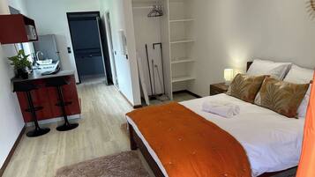 Quarto de hotel com cama, escrivaninha, cadeira, guarda-roupa e banheiro.