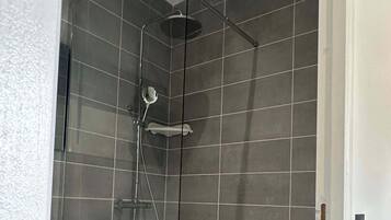A modern shower with a glass door, grey tiles, and a handheld showerhead.