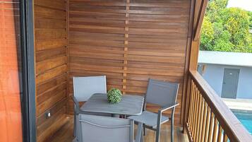 Eine Holzterrasse mit Tisch und Stühlen, Blick auf einen Swimmingpool und einem Holzgeländer.