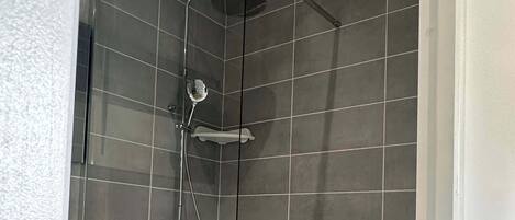 Une douche moderne avec une porte en verre, des carreaux gris et une douchette à main.