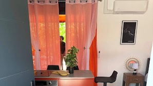 Une cuisine compacte avec un plan de travail rouge, une cuisinière et un évier. On y trouve un petit tabouret en bois et une lampe fixée au mur.