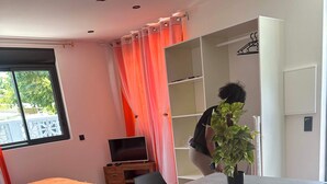 Une chambre d’hôtel moderne avec un lit, une petite télévision, un bureau agrémenté d’une plante et un mur d’accent rouge.