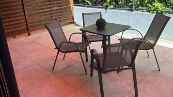 Um pátio externo com mesa e cadeiras, cercado por um muro de madeira e vegetação exuberante.