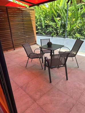 An outdoor patio with a table and chairs, surrounded by a wooden fence and lush greenery.
