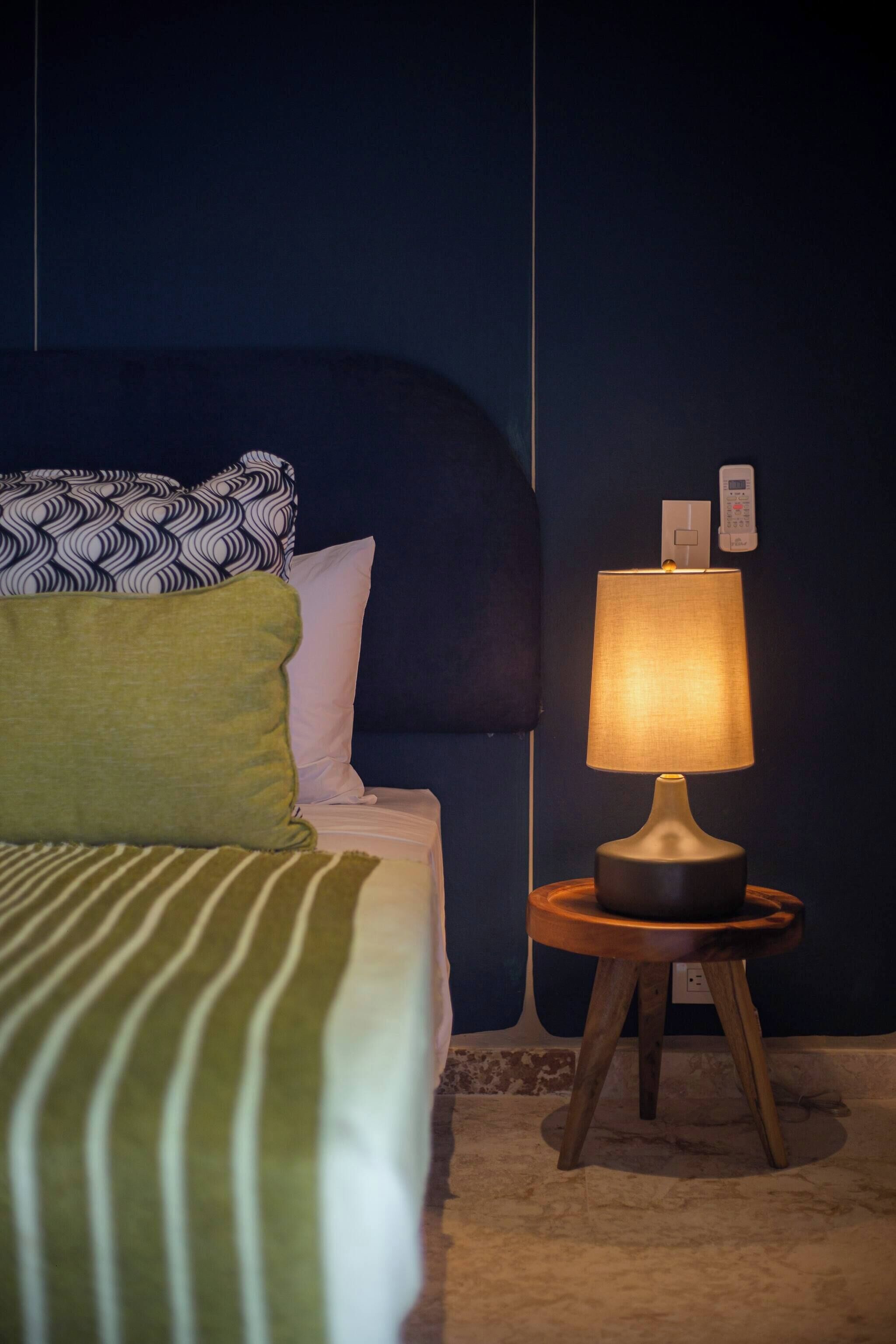 A neatly made bed with patterned pillows, a bedside lamp, and a wall-mounted thermostat.