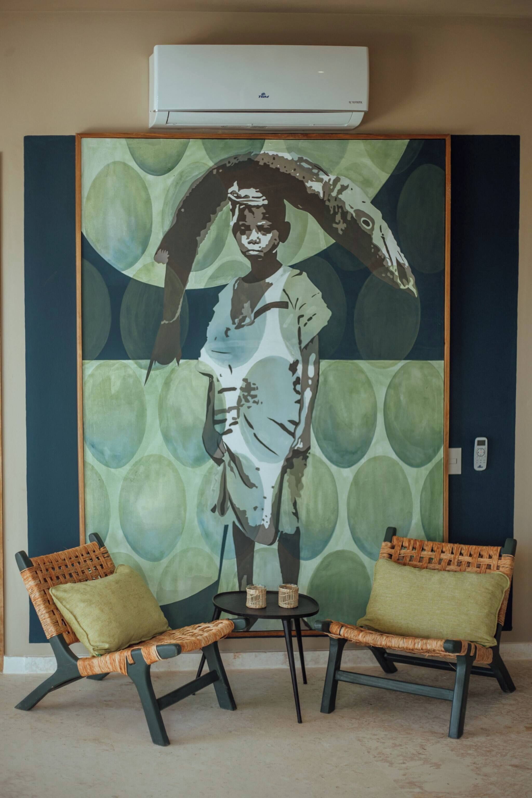 A room with a large wall mural, two wicker chairs with cushions, a small table, and an air conditioning unit.