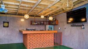 A bar area with a brick counter, shelves with bottles, a dartboard, and hanging lights. - Shose Campsite (Moshi)