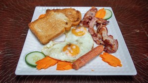 A plate of breakfast food including toast, eggs, bacon, sausage, and vegetables. - Shose Campsite (Moshi)