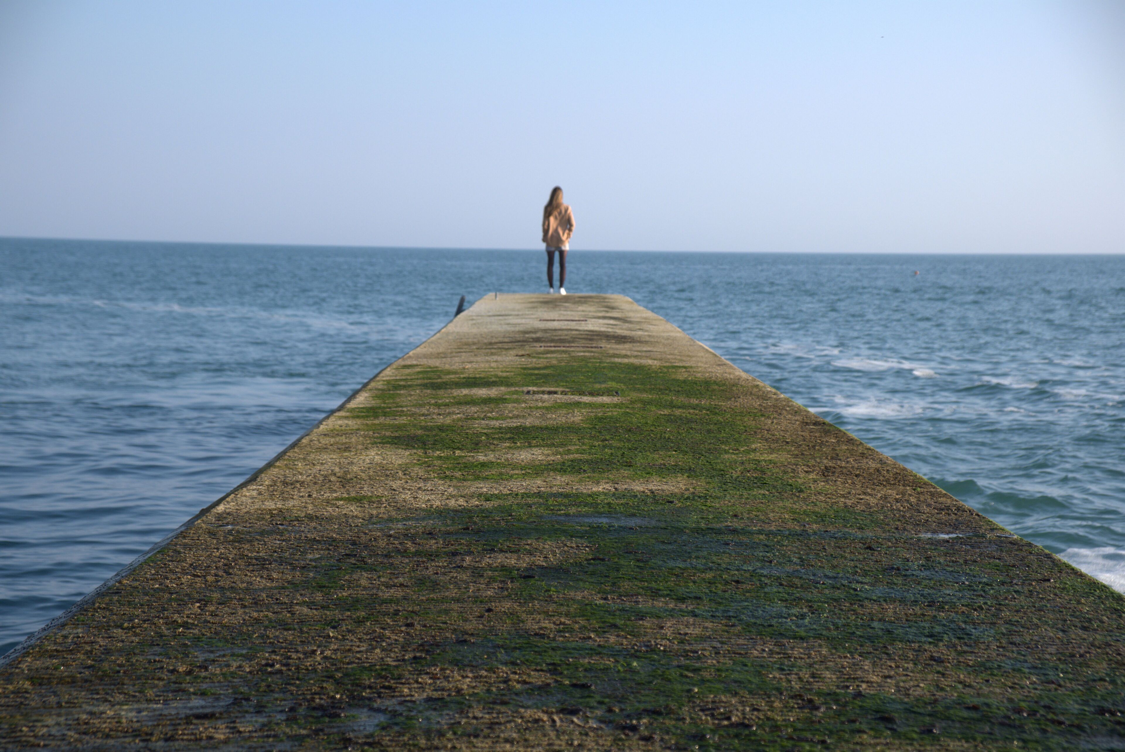 Une longue jetée s’étendant dans une étendue d’eau calme, avec une personne debout à son extrémité.