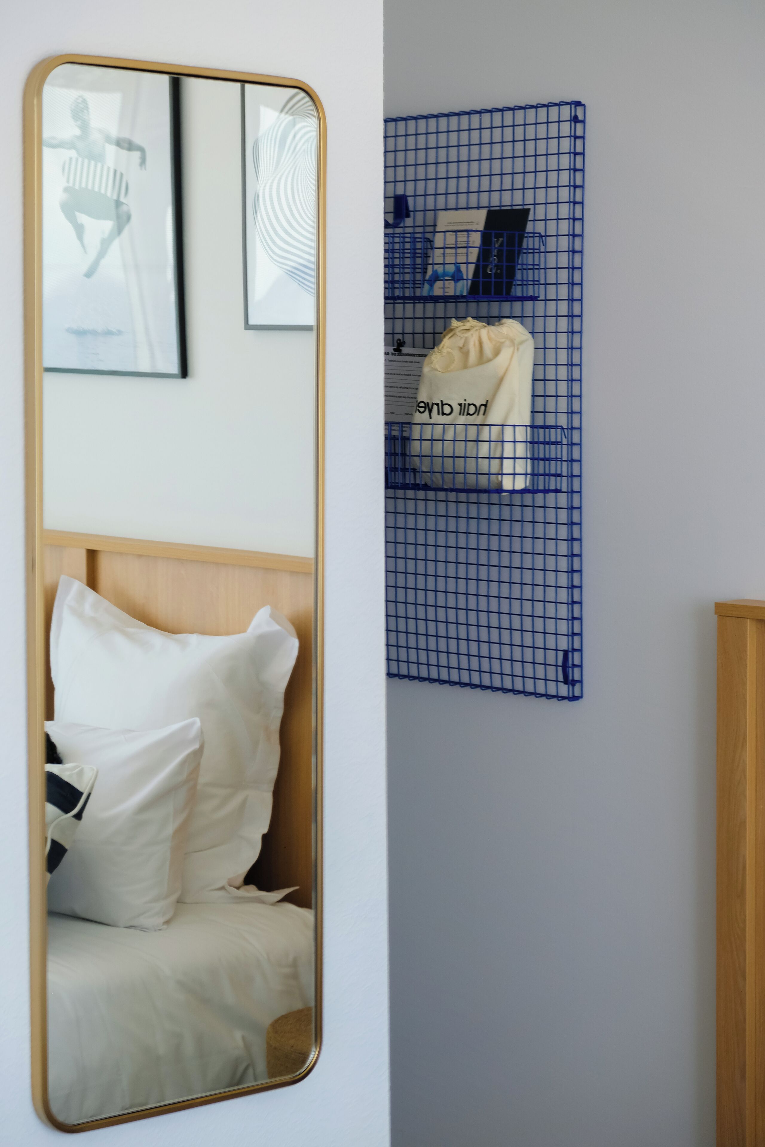 Un dormitorio con cama, un espejo grande, un organizador de pared azul tipo cuadrícula y un cabecero de madera.