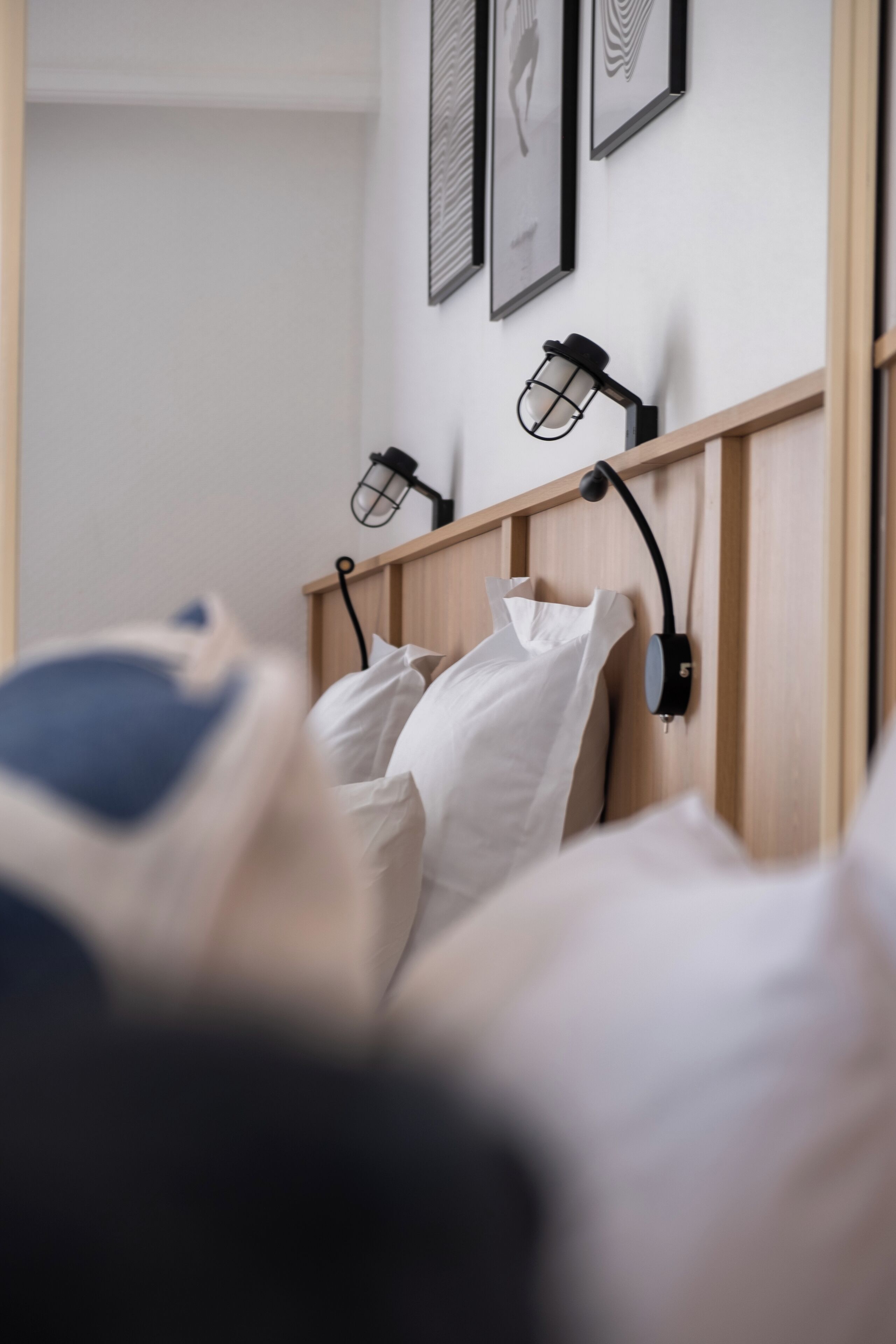 Un dormitorio con cabecera de madera, ropa de cama blanca y dos lámparas de lectura fijadas a la pared.