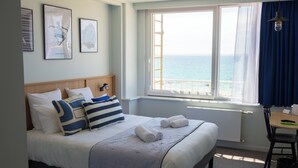Une chambre d’hôtel avec un grand lit, une vue sur la mer et des œuvres d’art accrochées au mur.