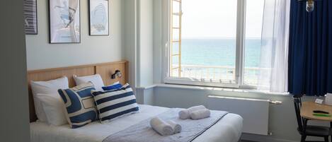 A hotel room with a large bed, a view of the sea, and artwork on the wall.